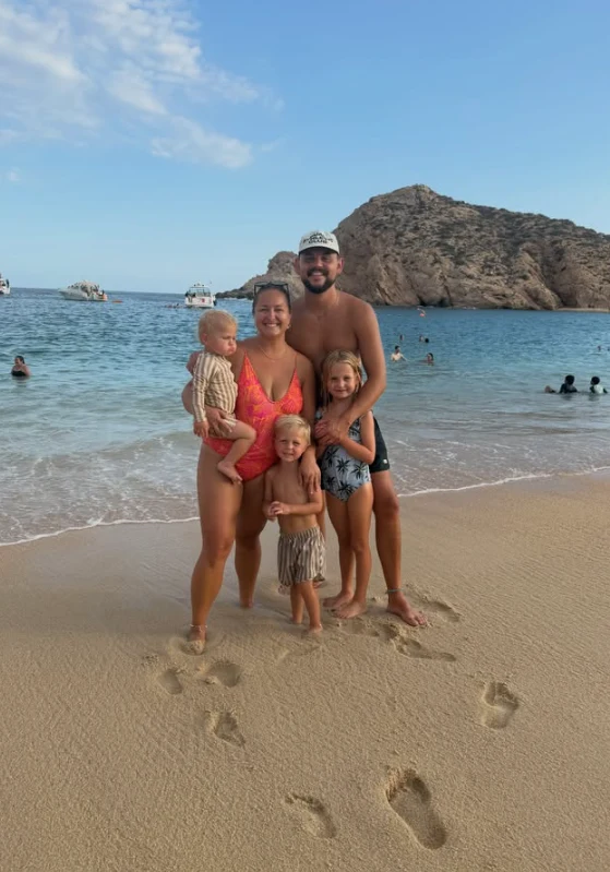Cory on the beach with his family, footprints in the sand behind them.