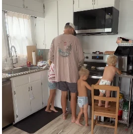 Cory cooking at the kitchen counter with two small children beside him.