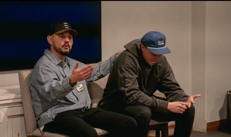 Cory in conversation with another man, both seated, mid-discussion in front of an audience.